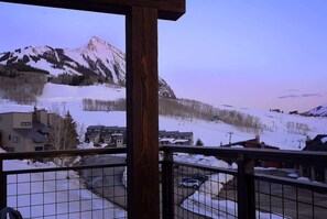 Une vue sur les montagnes depuis un balcon, avec un paysage enneigé et des bâtiments au premier plan.