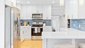 A modern kitchen with white cabinets, stainless steel appliances, a blue tiled backsplash, and pendant lighting. - Pelican Retreat ~ Screened-in Porch ~ Outdoor Shower ~ Large Back Yard ~ King (Wilmington)