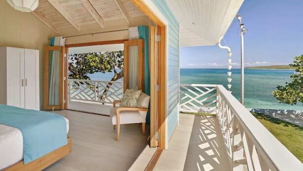 Ein Zimmer mit Bett, Sessel und einem Balkon mit Meerblick.