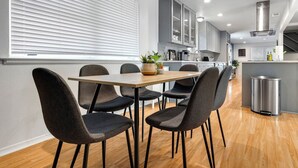 A modern kitchen with a dining area, featuring a wooden table, dark chairs, and a potted plant.