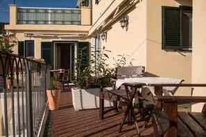 A balcony with outdoor furniture, potted plants, and a view of a building with green shutters.