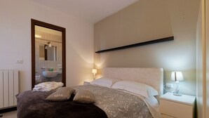 A bedroom with a bed, bedside tables, a nightstand, a mirror, and a bathroom visible through an open door. - Breathtaking view apartment with terrace 8 beds (Alassio)