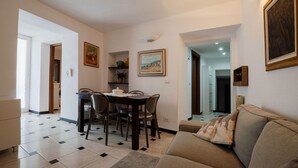 A living room with a sofa, a dining table with chairs, and a kitchen area in the background. - Breathtaking view apartment with terrace 8 beds (Alassio)