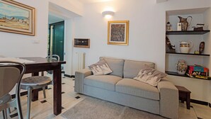 A living room with a sofa, a dining table with chairs, a framed picture on the wall, and a shelf with decorative items. - Breathtaking view apartment with terrace 8 beds (Alassio)