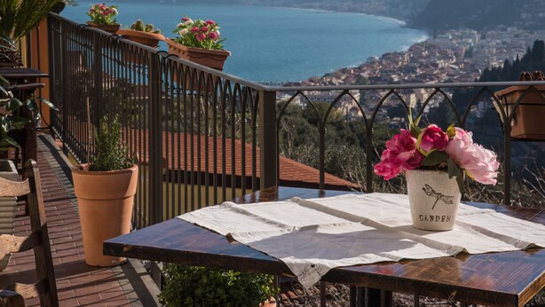 A terrace with a table, potted plants, and a scenic view of a lake and town. - Breathtaking view apartment with terrace 8 beds (Alassio)