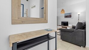 Una sala de estar moderna con un sofá gris, una mesa consola de madera, un espejo grande, una lámpara y un televisor.