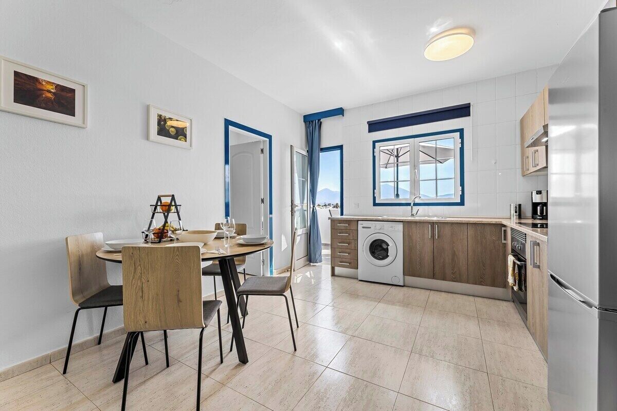 A modern kitchen with a washing machine, a dining area with chairs, and a view of the outdoors through a window.