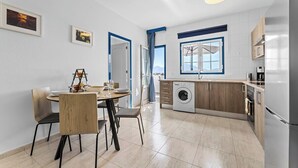 Cocina moderna con lavadora, comedor con sillas y vista al exterior a través de una ventana.