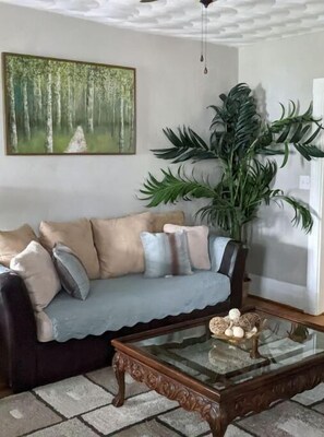 Relax in this inviting living room with a comfortable sofa, a beautiful painting, and a lush green plant.
