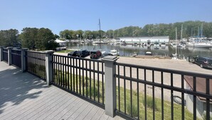 Un port de plaisance avec des bateaux amarrés, un grand bâtiment en arrière-plan et une terrasse en bois avec une rambarde en métal.