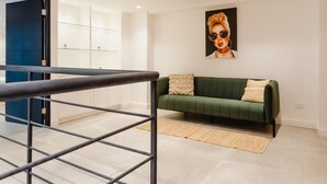 Un interior moderno con un sofá verde, piso de madera y una escalera con barandillas de metal.