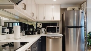 Una cocina moderna con electrodomésticos de acero inoxidable, armarios blancos y piso de baldosas.