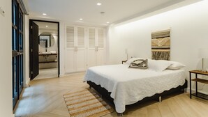 Un dormitorio con una cama grande, una mesita de noche, una lámpara de pared y una puerta que da al baño.