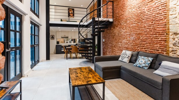 Un interior moderno con pared de ladrillo, una escalera, un sofá y un comedor.