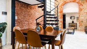 Un comedor con una mesa y sillas de madera, una escalera en espiral y una pared de ladrillo.