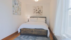 Une chambre à coucher comprenant un lit, une table de chevet, une lampe et deux œuvres d’art accrochées au mur.