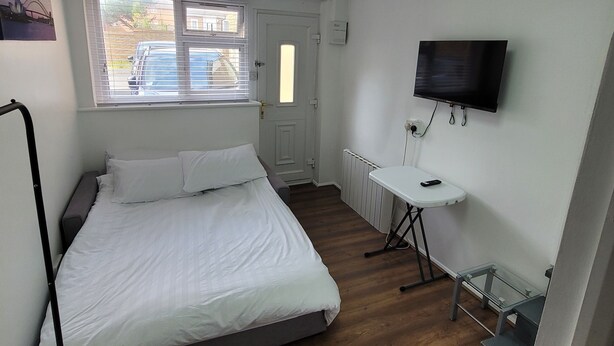 Un dormitorio con cama, escritorio, televisor, ventana con persianas y radiador.