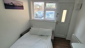 Un dormitorio con cama, ventana con persianas, radiador y puerta.