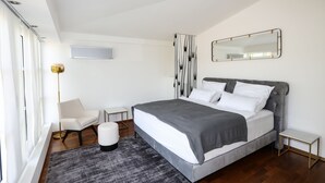 Un dormitorio moderno con una cama grande, una silla, una mesita y un espejo en la pared.