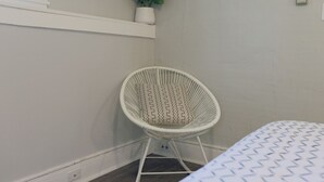 Ein Eckzimmer mit weißem Korbsessel, kleiner Topfpflanze und Bett mit gemustertem Überwurf.