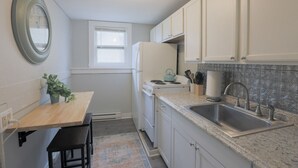 Eine kleine Küche mit weißen Schränken, einer Arbeitsplatte aus Granit, einem Spülbecken und einem kleinen Fenster.