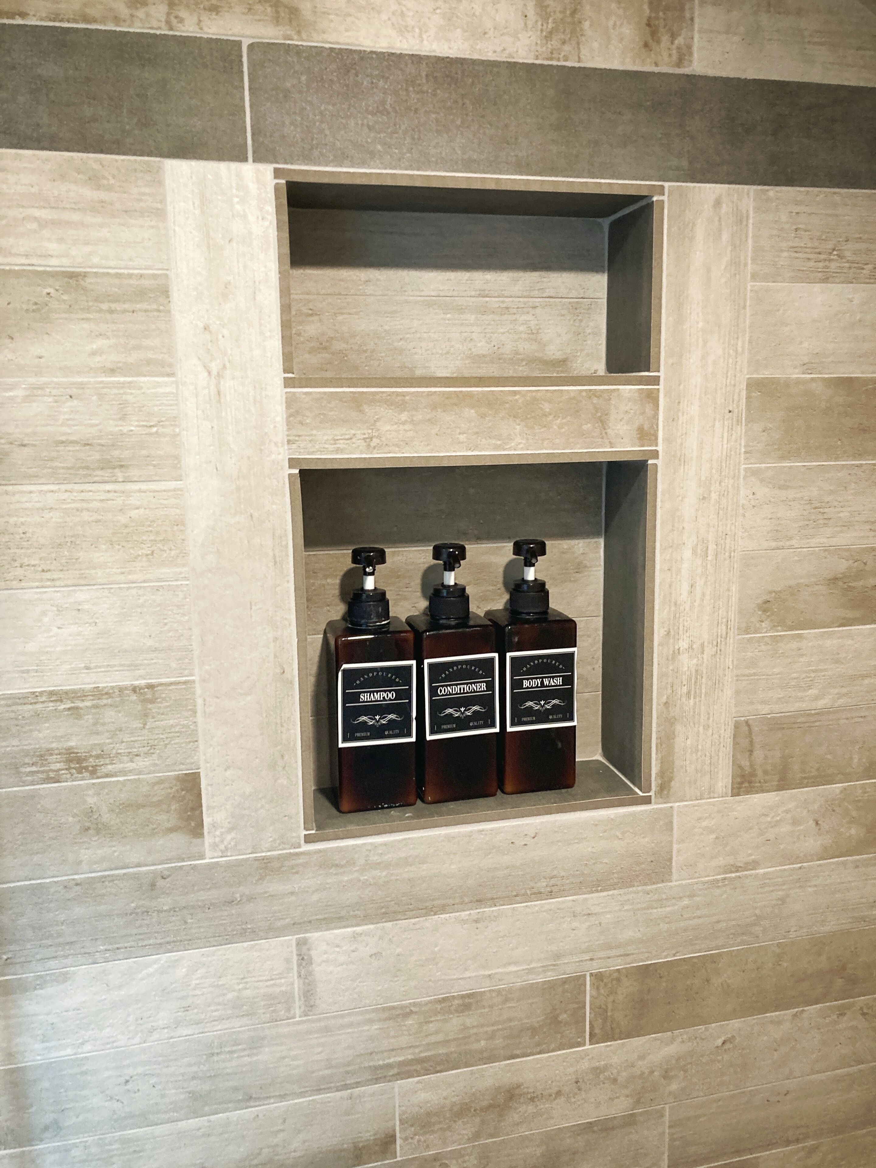 Une salle de bain avec un mur carrelé et trois flacons de produits de toilette placés sur une étagère.