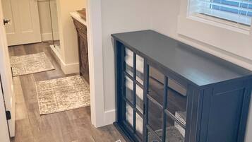A hallway with a dark wooden console table, a window with blinds, and a door leading to a bathroom.