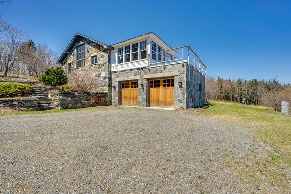 A two-story stone house with a stone staircase, a covered porch, and a fenced yard.