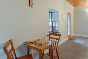 Ein Zimmer mit Holztisch, gedeckt für ein Spiel, zwei Holzstühle, einer Tür und einem Fenster.
