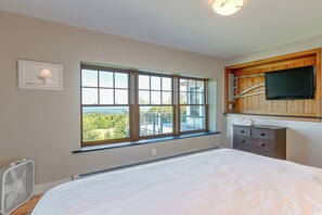 Ein Schlafzimmer mit einem großen Bett, einem Fenster mit Ausblick, einem an einer Holzvertäfelung montierten Flachbildfernseher und einem Nachttisch mit Lampe.