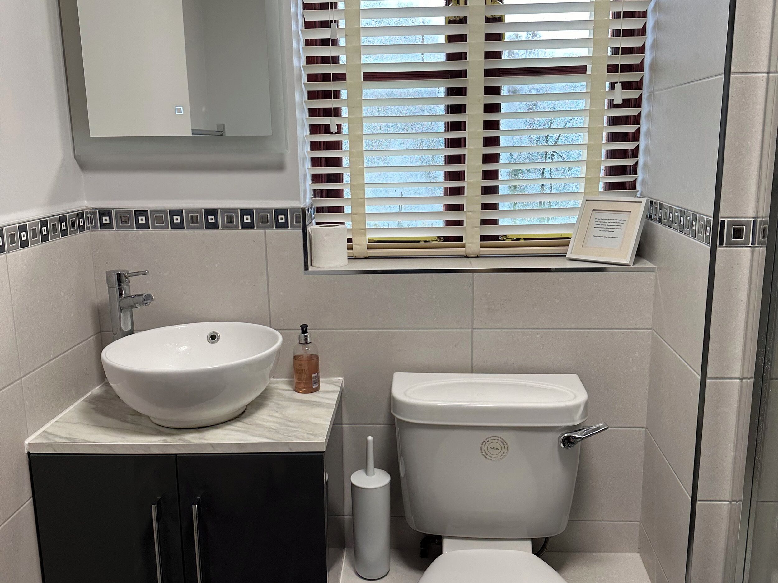 A bathroom with a white sink, toilet, and a window with blinds.
