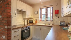 A kitchen with white cabinets, a microwave, a toaster, and a clock on the wall. - 10 Ruston Reaches (Norwich)