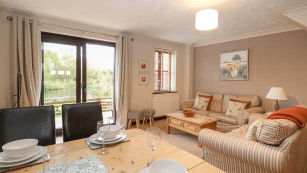 A cozy living room with a dining table set for two, a sofa, and a view of a garden through the window. - 10 Ruston Reaches (Norwich)