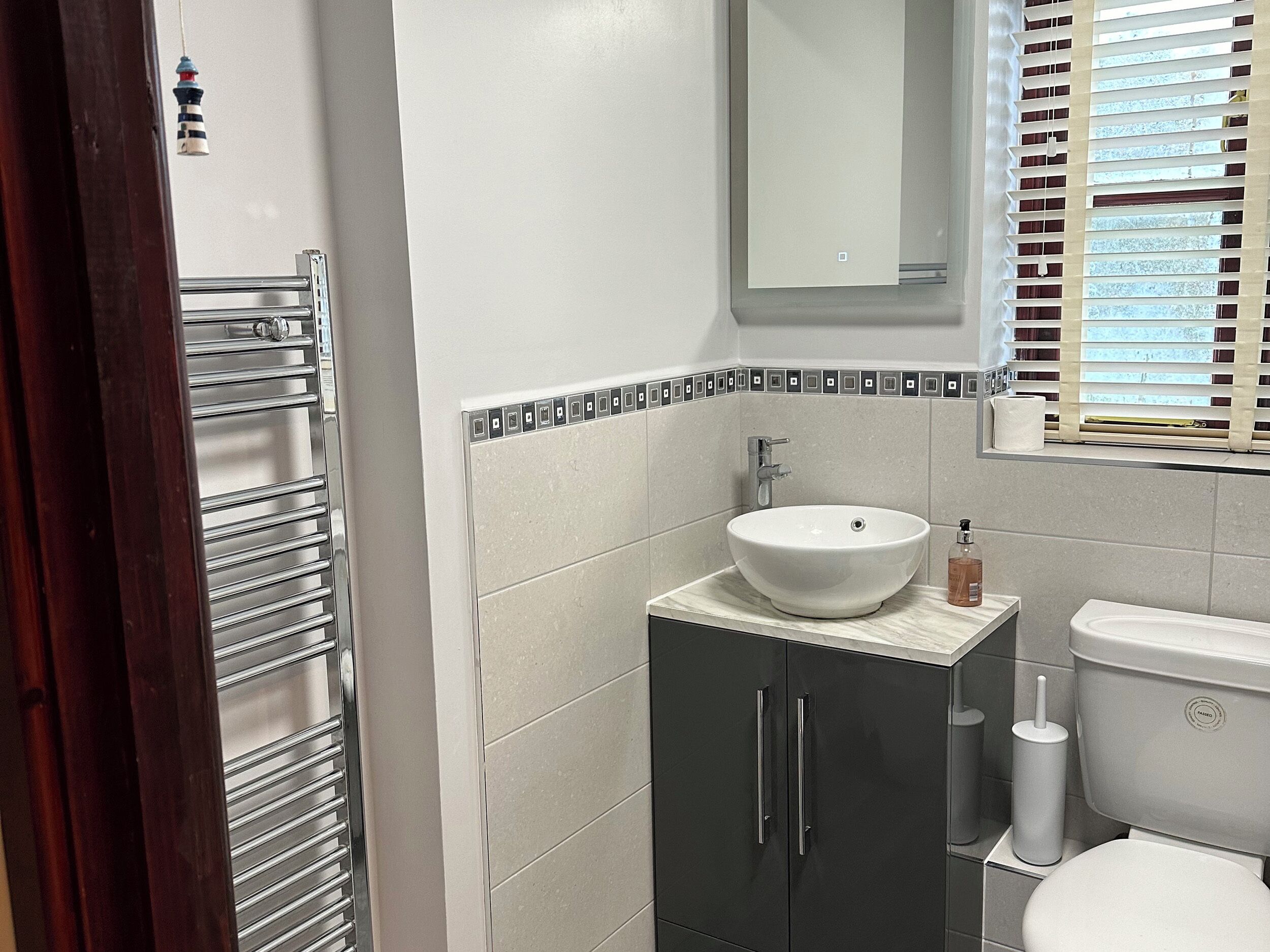 A bathroom with a white sink, dark cabinets, a toilet, and a window with blinds.