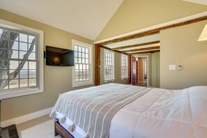A bedroom with a large bed, a flat-screen TV mounted on the wall, and a window with a view of trees. - Serene Retreat Near Mt Snow: Great for Groups! (Marlboro)