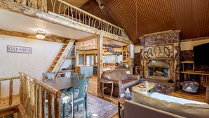 Een landelijk houten chalet interieur met een eethoek, een leren bank, een open haard en een trap naar een hoger niveau.