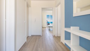 Ein Flur mit weißen Wänden und einer blauen Akzentwand, der zu einem Raum mit Meerblick führt.