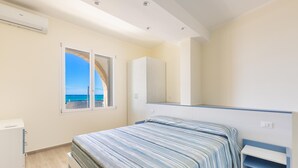 Ein Schlafzimmer mit Bett, Kleiderschrank, Schreibtisch und einem Fenster mit Meerblick.