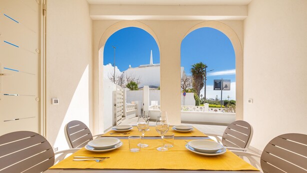 A dining area with a table set for four, white chairs, and a yellow tablecloth. - 3330 Appartamento Gemma Marina PT by Barbarhouse (Morciano di Leuca)