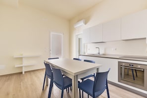 Una cocina moderna con armarios blancos, horno empotrado y comedor con mesa y sillas.