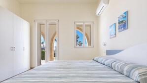 A bedroom with a bed, a wardrobe, and two windows with views of palm trees and a clear sky. - 3330 Appartamento Gemma Marina PT by Barbarhouse (Morciano di Leuca)