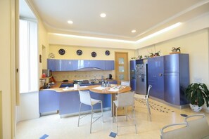 A modern kitchen with blue cabinets, a central island with chairs, and a refrigerator. - Panorama Suite (Vico Equense)