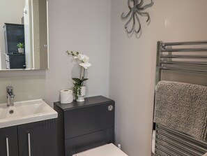 A bathroom with a white sink, dark cabinets, a toilet, a towel rack, and a decorative wall piece. - Spinnaker House (Scarborough)