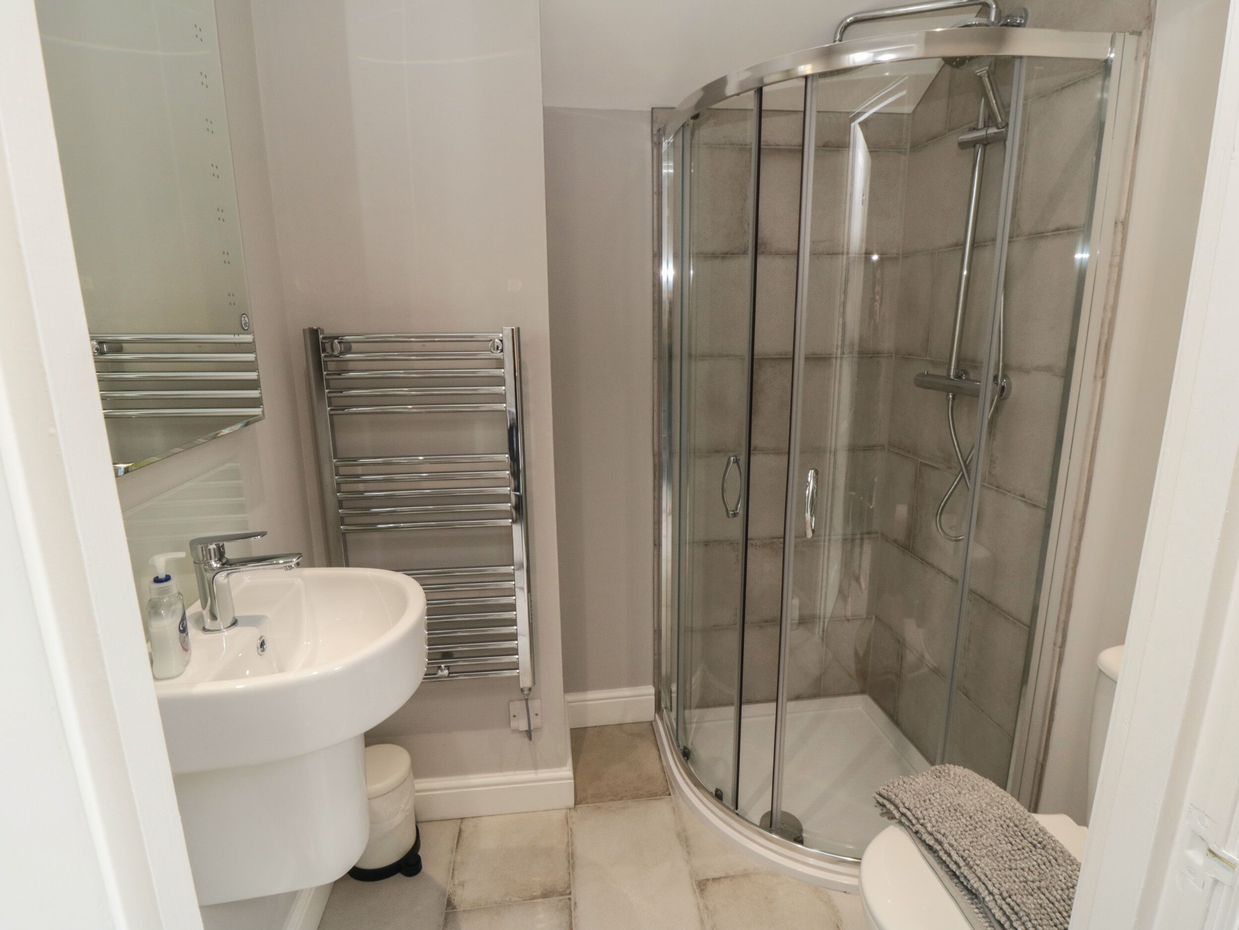 A modern bathroom with a glass-enclosed shower, a white sink, and a chrome towel rack.