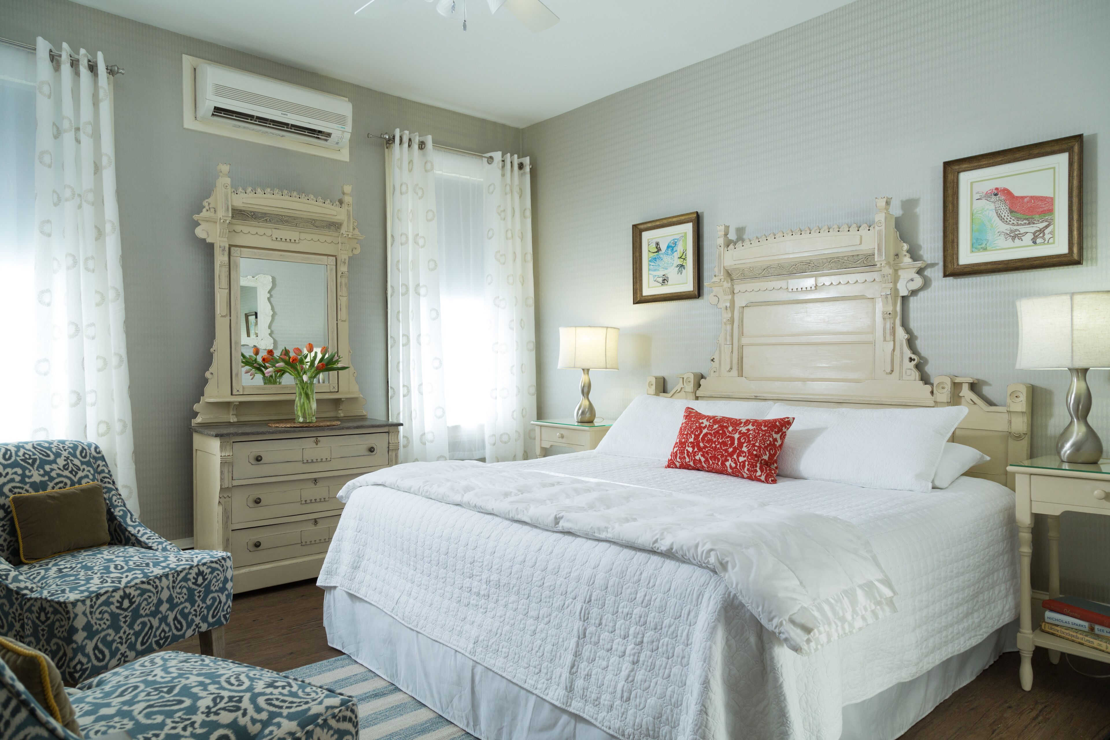 A bedroom with a large bed, a dresser, a chair, and a nightstand with lamps.