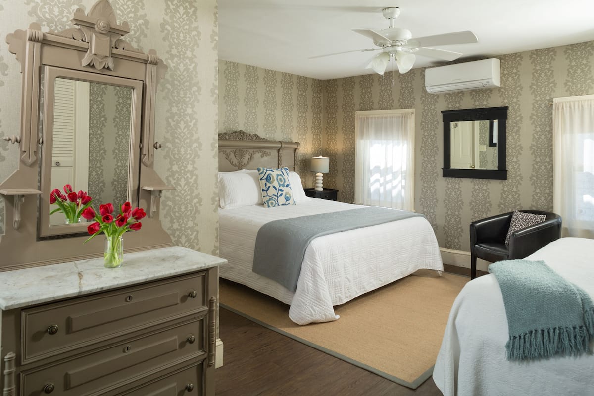A bedroom with a large bed, a dresser, a vanity, and a mirror.