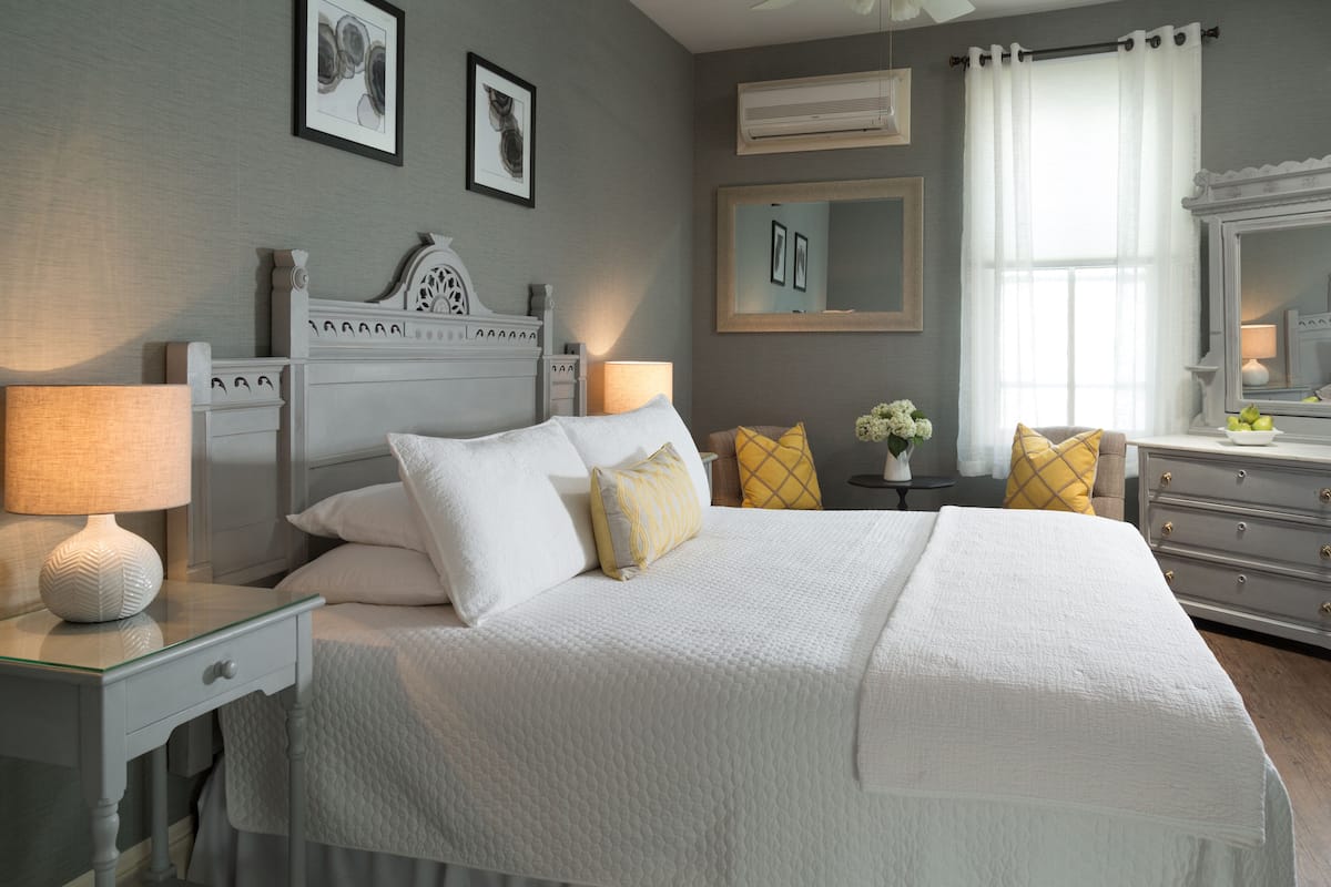 A neatly arranged bedroom with a bed, bedside tables, a dresser, and a mirror.