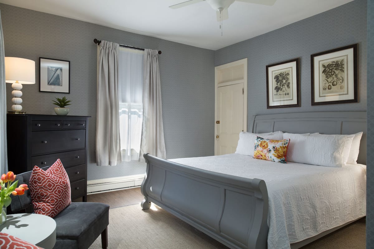 A bedroom with a bed, a dresser, a chair, a lamp, and a window with curtains.