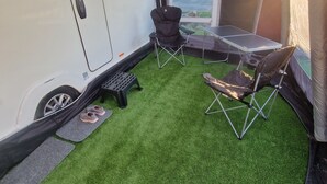 A camper with an openable door, a foldable table, two chairs, and artificial grass flooring. - Swift Vogue Edition Caravan (Holyhead)