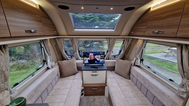 A cozy RV interior with a central seating area, a TV, and large windows offering scenic views. - Swift Vogue Edition Caravan (Holyhead)